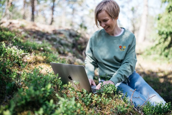 Nainen istuu metsässä kannettava tietokone sylissään