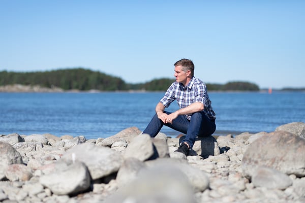 Mies istuu kivikkoisella merenrannalla aurinkoisena päivänä