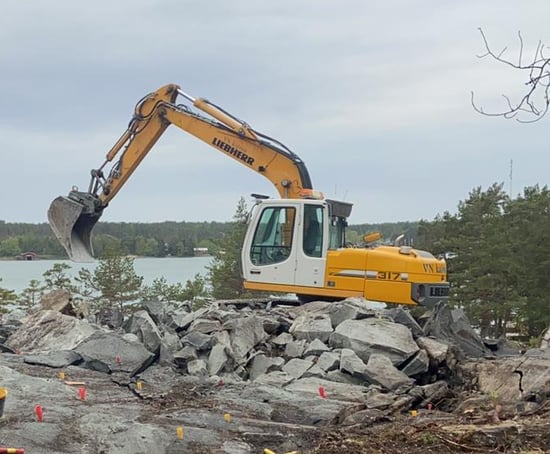 Kaivinkone kaivamassa räjäytetun kallion kivilohkareita.
